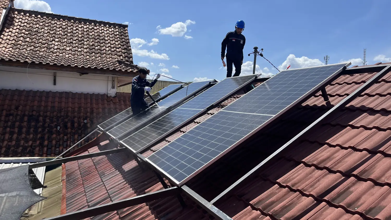 Dua teknisi Ufuk Hijau Energi membersihkan panel surya di atap